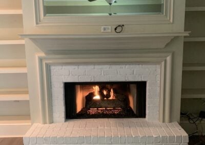 small white fireplace with gas logs and large mirror